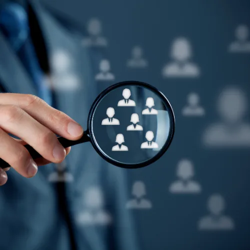 A hand holding a magnifying glass over a group of customer icons